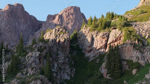 Warm sunlight gradually illuminates the rugged mountain peaks and lush green slopes, creating a captivating display of nature's beauty and tranquility