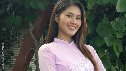 Beautiful Asian woman with long hair in pink Vietnamese dress smiling and looking at the camera, 4K video.