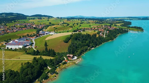 Forggensee lake with turquoise water, green fields, and roads winding through the Bavarian Alps near Rieden am Forggensee. Captured from drone on a sunny summer day