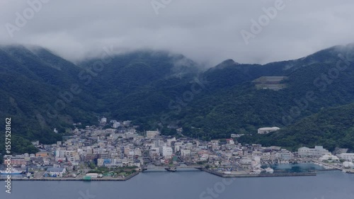 Aerial rotation around harbor town by foggy coastal mountains - Setouchi, Amami Island, Japan