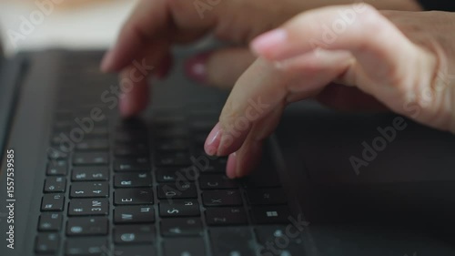 Close up of woman typing on laptop keyboard with fingers having pink painted nails, captured in soft blur background, emphasizing motion and focus during digital work environment indoors