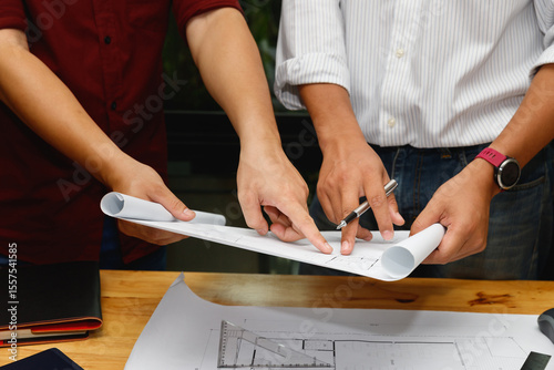 Close-up of two architects discussing a blueprint on a desk. Concept of teamwork, architecture planning, engineering, and professional collaboration.