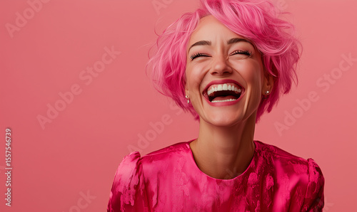 Modern adult woman in stylish pink clothes with pink hair, laughs very hard. Portrait of a happy woman on a pastel pink background. Copy space for banner.