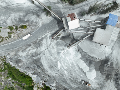 Aerial view of granite and limestone crushing plant with dump trucks and excavators processing raw stone into construction aggregates for concrete and infrastructure development. Stone mill factory.