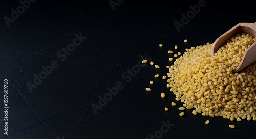 Yellow grains spilling from wooden scoop on dark background  