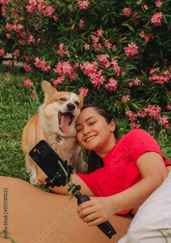 Young girl with Corgi recording video on phone share via app her travel vacation. Gen Z influencer shooting social media stories. Concept of friendship between a dog and human. Part of a series. UGC
