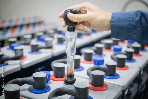 Technician inspects backup battery power system using hydrometer to ensure optimal performance and safety in industrial environment with multiple connected batteries