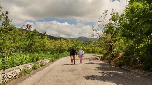 A man and a woman are leisurely walking down a road surrounded by natures beauty and tranquility
