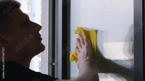 A man wipes a dirty window in a house with a rag.
Cleaning the apartment.
A cleaner with a rag wipes dirt and dust on the window