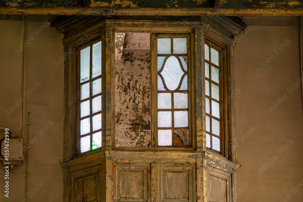 Obraz premium Weathered wooden observation booth with stained glass windows, built into the wall of an old, decaying building. Peeling paint and signs of neglect emphasize a vintage, abandoned atmosphere.