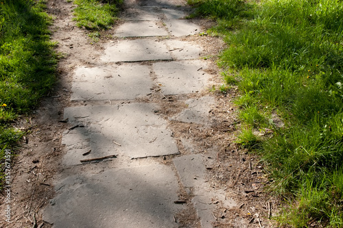 Old cracked walkway made of scattered tiles leads into the distance, with green grass growing along both sides — a quiet, slightly overgrown path.