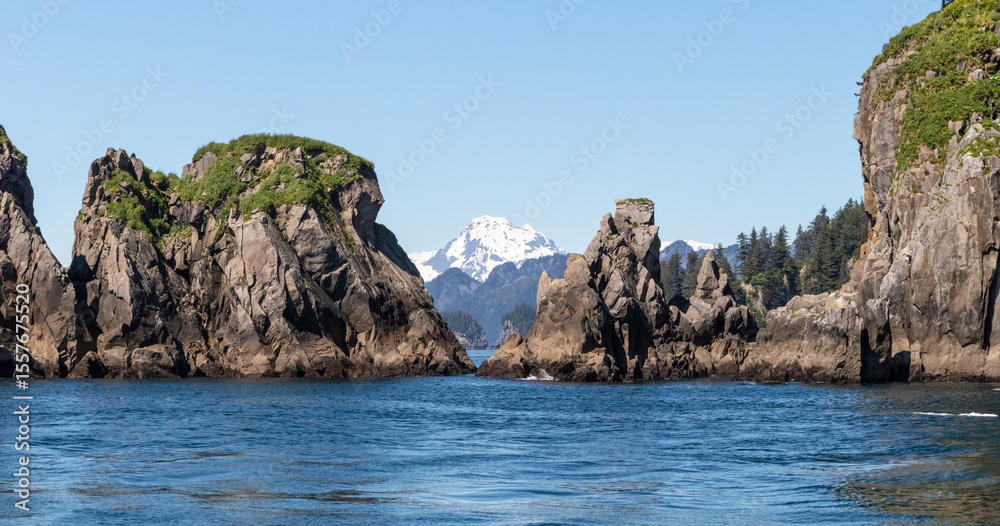 Naklejka premium A view from the water of rock formations and a snow covered mountain in the distance in Alaska