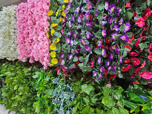 Rows of vibrant artificial flowers and lush green plants in a store, perfect for home decor, events, or crafts.
