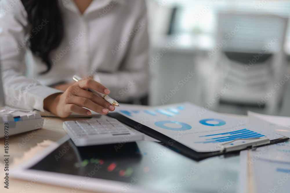 Fototapeta premium Businesswoman working with financial data using calculator and digital tablet, analyzing charts and graphs