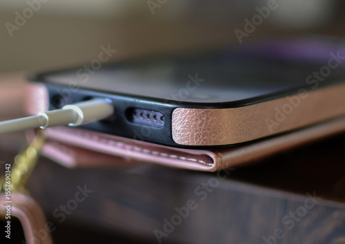 Smartphone in a pink case connected to a charger, charging on a wooden table.

