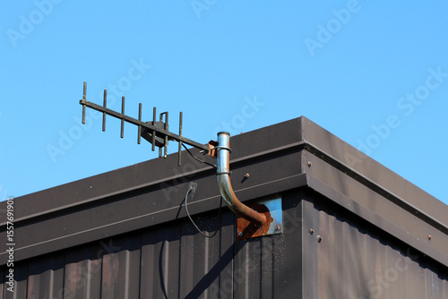 A directional tv antenna with multiple elements is fixed to a rusted metal bracket on a modern building’s roof, set against a cloudless blue sky for optimal signal reception