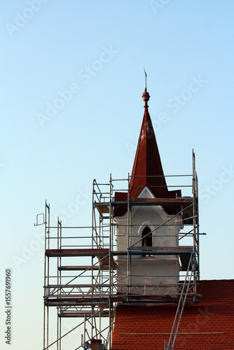 Red spire of old church tower surrounded by metal scaffolding, highlighting ongoing restoration work and architectural preservation under a blue sky