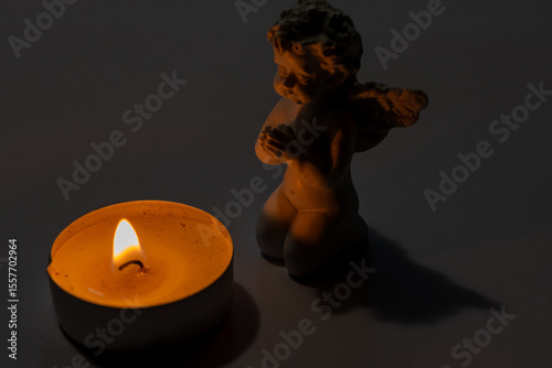 A ceramic angel figurine kneeling beside a lit tealight candle in a dark, peaceful setting. Symbol of prayer, remembrance and spirituality.