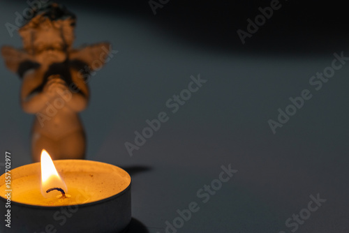 A ceramic angel figurine kneeling beside a lit tealight candle in a dark, peaceful setting. Symbol of prayer, remembrance and spirituality.