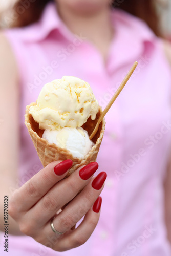 Girl with ice cream in waffle cone. Tasty ice cream in waffle cone in female hands. Eating ice cream outdoors. Summer background. Two ice cream balls in waffle cone with spoon. Tasty frozen dessert