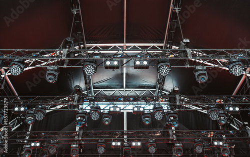 Close-up view of a dense lighting grid structure with an array of mounted LED wash lights, moving head fixtures, and trusses under a dark stage canopy, prepared for a high-energy live event