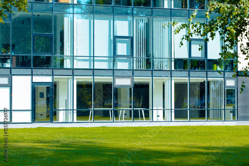 modern office exterior glass wall and windows material facade summer bright vivid day time view perspective building background and green foliage nature foreground