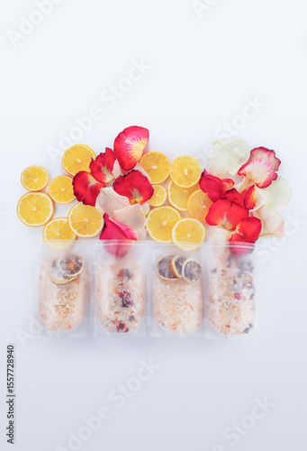 Freshly prepared snacks arranged on a light surface showcase vibrant slices of lemon and elegant rose petals, creating a visually appealing display. Each snack is wrapped in translucent packaging, rev