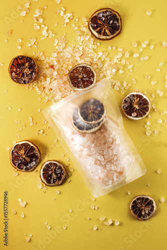 collection of dried lemon slices surrounding a transparent bag filled with coarse salt scattered on a vibrant yellow background, creating an eye-catching arrangement that highlights the contrast betwe