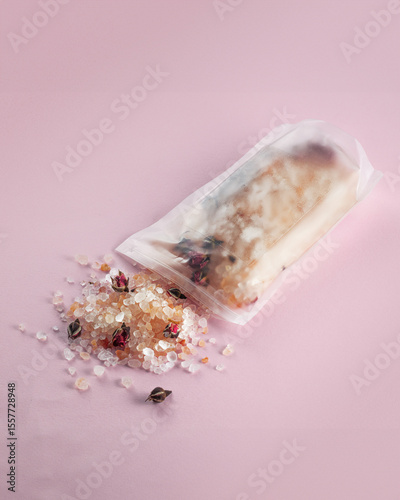 bath salt package lies on a soft pink surface, with some of its contents spilling out. The bath salts, infused with rose petals and herbs, create a luxurious and relaxing atmosphere for a self-care ro