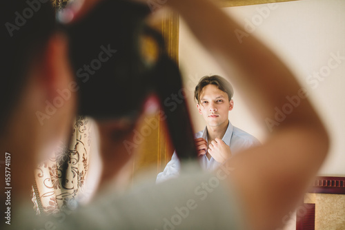 Caucasian man adjusting shirt collar before a photoshoot, seen through photographer’s arms — authentic behind-the-scenes moment showing focus, style, and creative preparation.