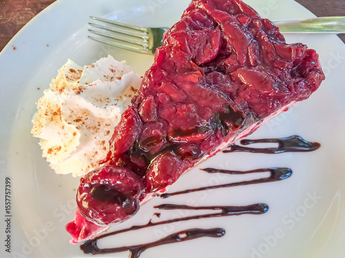 A slice of cheesecake with cherry sauce on a white plate, decorated with cream
