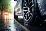 Close up of a car wheel driving on a wet road during a rainy day in the city, with blurred traffic lights in the background
