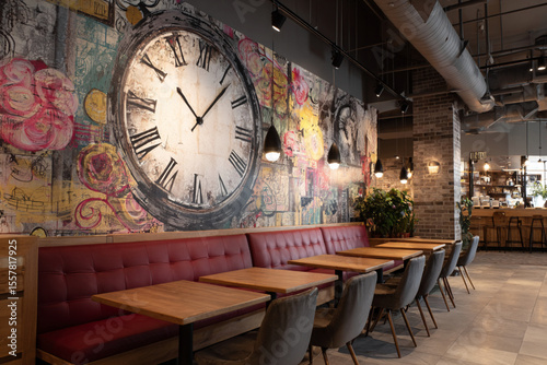 Cozy dining area with vibrant mural and stylish clock featuring wooden tables and upholstered seating in a modern restaurant