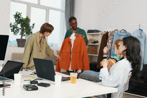 Young adult woman and coworkers socializing at workplace, discussing business ideas and clothing with friends, representing Gen Z work environment and collaboration.