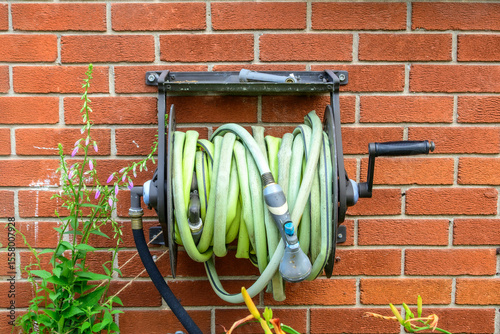 garden hose (sun faded green with nozzle) reeled into spool on a red brick wall