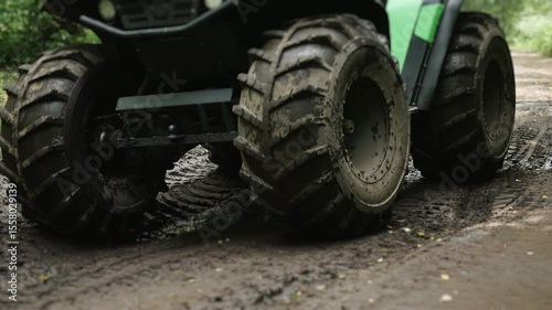 Close-up of powerful wheels of quad bike driving on rural road in mud. Off-road vehicle driving on road washed out by rain.