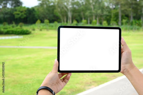 Hands holding digital tablet with blank screen outdoors, ideal for mockup or app promotion in a natural