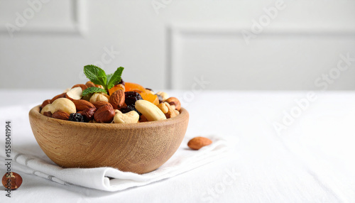 Nuts and dried fruit mix in a round bowl of wood against a rough white background.