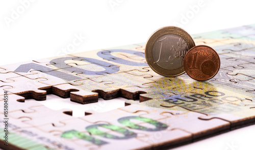 A 100 euro note made from puzzle pieces, 1 euro and 1 euro cent coins on a white background