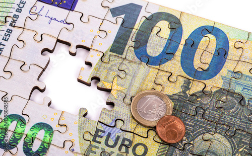 A 100 euro note made from puzzle pieces, 1 euro and 1 euro cent coins on a white background