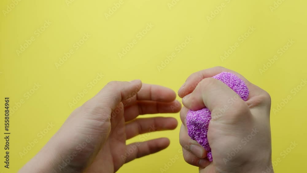 Close-up of hands squeezing and shaping purple floam slime on a bright yellow background, highlighting sensory play and tactile stress relief, demonstrating the texture and malleability, static shot