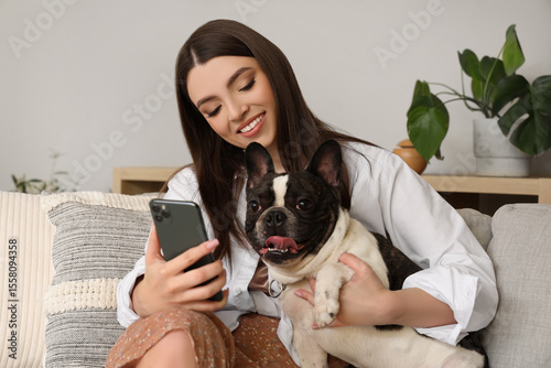 Young woman with her French bulldog using mobile phone at home