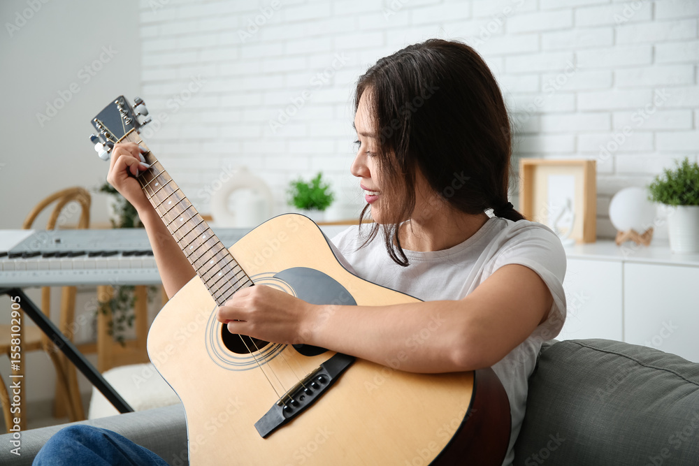 Fototapeta premium Pretty young woman playing guitar at home
