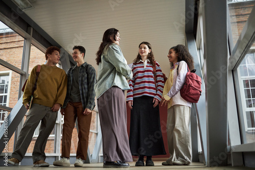 Group of multiethnic university students standing in hallway talking and smiling, young adult men and women interacting together, casual conversation during break between classes
