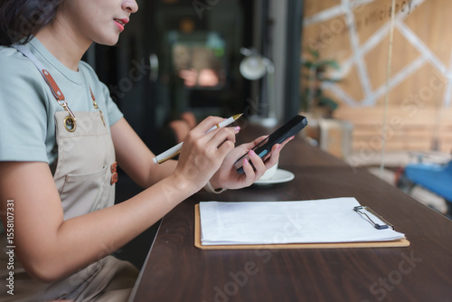 Coffee shop owner managing inventory and orders using smartphone and clipboard