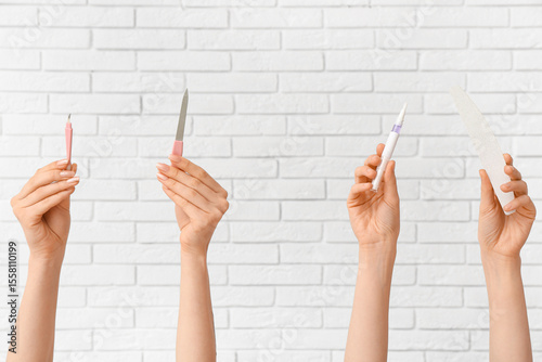 Female hands with cuticle oil pen, nail files and cutter on white brick background