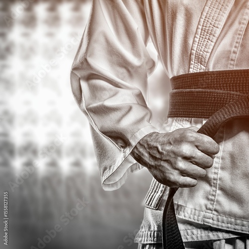 Midsection of martial artist tying black belt on uniform