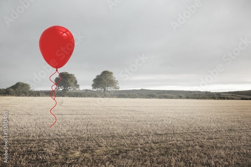 Red helium balloon is floating above stubbled farmland in flat design under overcast sky