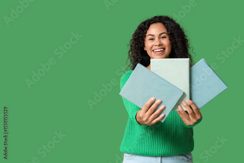 Happy young African-American woman with books on green background