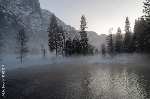 An eerie mist covers the floor of yosemite valley, while a thin layer of snow outlines the trees in during a beautiful sunset.
